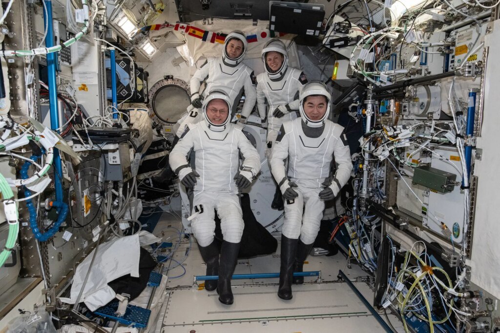 Four SpaceX Crew-11 members gather together for a crew portrait wearing their Dragon pressure suits during a suit verification check inside the International Space Station