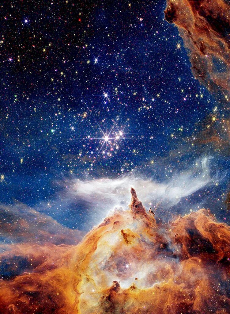 A winter scene fit for a holiday greeting card. Above what appears to be a fantastical snowy mountainscape, is a brilliant blue sky packed with colorful lights. The golden mountainscape is in fact part of the nebula NGC 6357, as captured by NASA