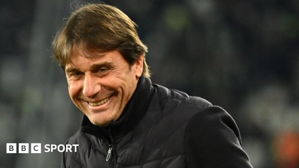 Head and shoulders view of a smiling Antonio Conte in a black, zipped-up jacket