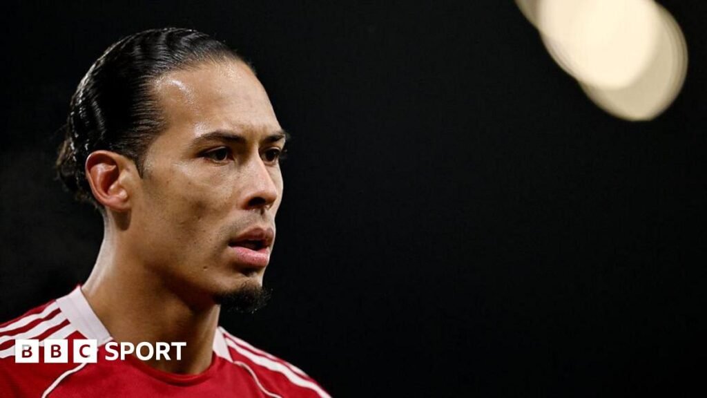 Close-up image of Virgil van Dijk in the left of the photograph. He has black hair, tied back, and is wearing Liverpool